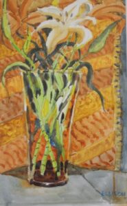 a bunch of white lilies in a glass vase with a backdrop of orange tapestry